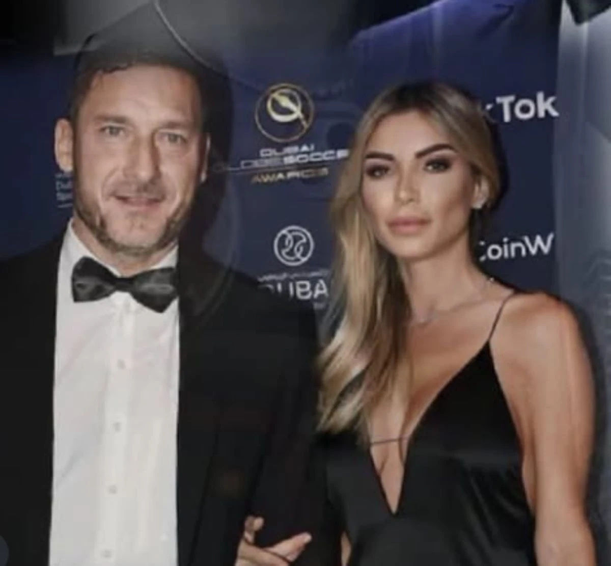 Francesco Totti e Noemi Bocchi sorridenti al battesimo di Diego, circondati dai familiari